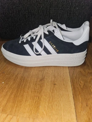 Gazelle Bold W Sneakers - Svart - EUR 39 1/3 - Säljer ett par nästan helt nya Adidas Gazelle Bold W i den klassiska svarta färgen med vita detaljer. Jag köpte dem förra sommaren men de har tyvärr bara blivit stående i garderoben då de är lite för stora för mig.  Skorna är endast använda två gånger och är därför i fantastiskt fint skick. Detta är den populära "Bold"-modellen med en snygg platåsula i tre lager.