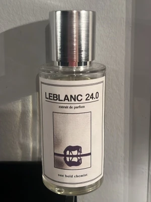 LEBLANC 24.0 Parfym One Bold Chemist - En stilren parfymflaska i glas med metallock från One Bold Chemist. Doften heter LEBLANC 24.0 och är ett extrait de parfum. Flaskan är genomskinlig med en minimalistisk etikett i vitt och svart, och innehållet är ljust gult.