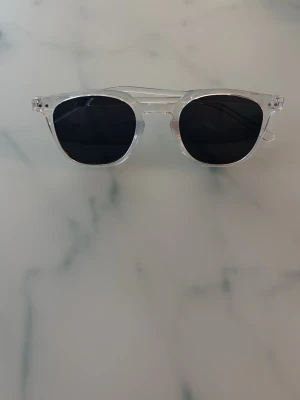 Transparenta solglasögon med svarta glas - Snygga solglasögon med transparent båge och mörka, svarta glas. Klassisk rundad form som passar till de flesta stilar. Lätta och bekväma att bära, perfekta för soliga dagar.