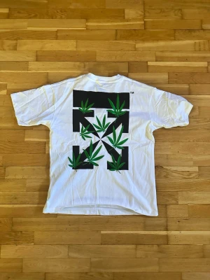 Vit Off-White t-shirt med broderi - Vit t-shirt från Off-White med stort svart grafiskt tryck och broderade gröna blad på ryggen. Klassisk passform och korta ärmar. Materialet är mjuk bomull och detaljerna gör den riktigt unik.