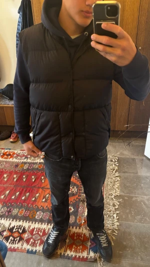Svart dunväst med huva - Säljer en svart dunväst från Vailent med hög krage och huva.  Har en liten krigs skada längst ner eftersom knappen lossna, har knappast använt västen eftersom jag köpte en storlek för stor är 170-65kg