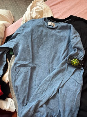 Blå Stone Island tröja - Snygg blå tröja från Stone Island med klassisk rund hals och den ikoniska loggan på ärmen. Tröjan är tunnstickad och har en stilren design som passar perfekt. Passar s/M