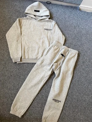Grå mjukisbyxor från Essentials - Snygga grå mjukisbyxor från Essentials med broderad logga vid benet. Byxorna har resår i midjan med dragsko och muddar vid bensluten. Tillverkade i mjukt och bekvämt material, perfekta för en avslappnad stil.