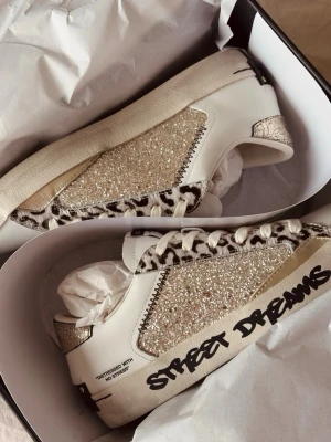 Glittriga sneakers från Crime London - Snygga sneakers från Crime London med glittriga paneler i guld, leopardmönstrade detaljer och texten 'Street Dreams' på sulan. Skorna är helt nya, säljer då de inte passade. Storlek 37😊