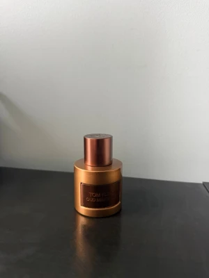 Tom Ford Oud Minérale parfym - Lyxig parfym från Tom Ford i modellen Oud Minérale. Flaskan är rund och har en snygg metallisk kopparfärg med matchande lock. Märkets logga och namn syns på en metallplatta framtill. Perfekt för dig som gillar exklusiva dofter och stilren design.