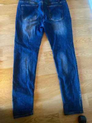 Blå slim fit jeans med slitningar - Snygga blå slim fit jeans med slitna detaljer och klassisk femficksdesign. Jeansen har en något tvättad look med ljusare partier framtill och bakfickor. Perfekta för en avslappnad och trendig stil.