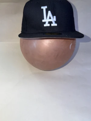 Svart LA-keps från New Era - Snygg svart keps från New Era med LA Dodgers-logga broderad i vitt framtill och MLB-logga bak. Klassisk flat brim och stilren design, perfekt för dig som gillar streetwear. Tillverkad i bomullsmix för skön passform.