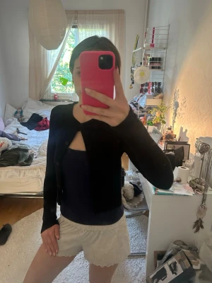Svart cropped kofta med knappar - Snygg svart cropped kofta med rund halsringning och knäppning framtill. Modellen är figurnära och har långa ärmar. Perfekt att styla över ett linne eller t-shirt för en trendig lager-på-lager-look.