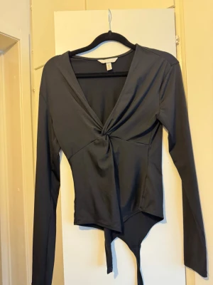 H&M body svart strl S - Svart långärmad body med en knuten detalj framtill. Bodyn har en V-ringning och en figurnära passform.