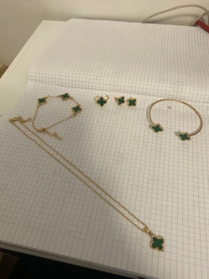 Guldhalsband med grön fyrklöver - Snyggt halsband i guldton med ett hänge i form av en grön fyrklöver. Hänget har en dekorativ pärlkant runt om och kedjan är tunn och elegant. Perfekt för dig som gillar unika detaljer och vill sticka ut med ett färgglatt smycke.