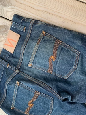 Nudie Jeans LOW SLIM JIM Discontinued  - Riktigt feta nudie jeans i den  sällsynta modell en "LOW SLIM JIM". Modellen är discontinued och säljs inte längre vilket man tydligt kan se på patchen på jeansen paksida. W29 men utgå alltid från angivna mått! Midja: 39, Ytterben: 105, Innerben: 78, Benöppning: 20