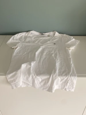 Vit v-ringad t-shirt från Gant - Klassisk vit t-shirt från Gant med v-ringning och liten broderad logga på bröstet. Tillverkad i mjuk bomull och har korta ärmar. Perfekt basplagg för alla tillfällen och enkel att matcha med olika stilar.