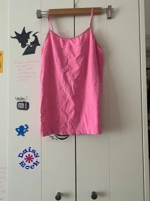 Rosa linnetopp med smala axelband - Snygg rosa linnetopp med smala axelband och enkel design. Perfekt att styla med jeans eller kjol för en trendig look. Tillverkad i mjuk bomull som känns skön mot huden.