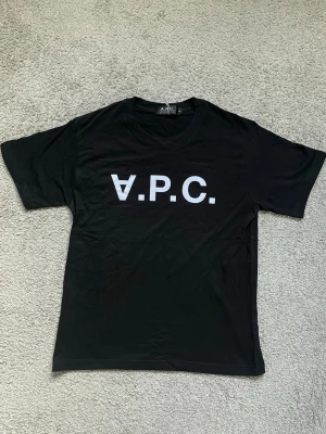 Svart A.P.C. t-shirt med tryck - Snygg svart t-shirt från A.P.C. med stort vitt logotryck på bröstet. Klassisk rund hals och korta ärmar. Tillverkad i mjuk bomull som känns skön mot huden. Perfekt för dig som gillar stilrena och trendiga plagg.