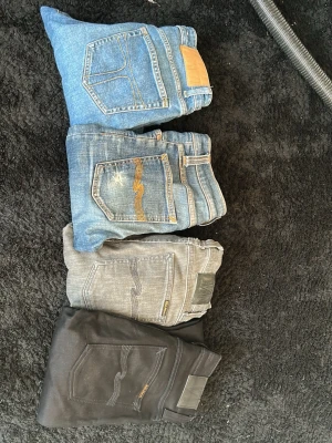 Fyra par jeans från Nudie Jeans - Säljer fyra par Nudie Jeans i olika färger: ljusblå, mellanblå med slitningar, grå och svarta. Alla har klassisk femficksmodell och Nudie Jeans signaturdetaljer på bakfickan. Tillverkade i ekologisk bomull och återvunnen elastan för skön stretch.eba och ena paret har slitningar på sig som är så i modellen