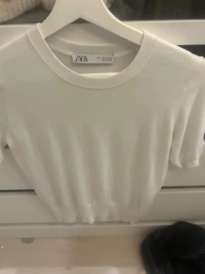 Vit kortärmad topp från Zara - En stilren vit topp från Zara med rund halsringning och korta ärmar. Tillverkad i mjukt material som känns skönt mot huden. Perfekt att matcha med jeans eller kjol för en clean look.