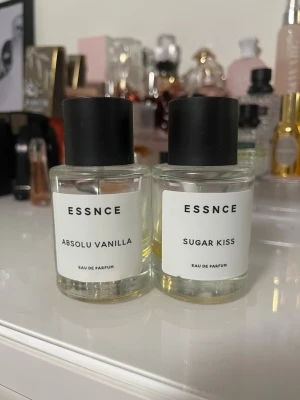ESSNCE Absolu Vanilla & Sugar Kiss - Två parfymer från ESSNCE: Absolu Vanilla och Sugar Kiss. Båda kommer i genomskinliga, runda glasflaskor med svarta lock och minimalistiska vita etiketter. Doftvätskan är ljusgul. Perfekt för dig som gillar söta och mjuka dofter.