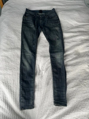 Mörkblå skinny jeans med slitningar - Säljer ett par mörkblå skinny jeans med snygga slitningar och tvättade detaljer. Jeansen har klassisk femficksmodell, låg midja och smala ben. Perfekta för dig som gillar en tight passform och en trendig look.