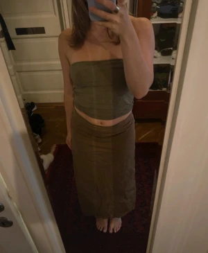 Olivgrön bandeau tubtopp i linne - Säljer en enkel och stilren olivgrön bandeau tubtopp i linne. Toppen är axelbandslös och croppad, perfekt för varma dagar eller att styla med en kavaj. Superskön passform och lätt att matcha med olika underdelar. ”Handtaget” till dragkedjan är sönder men dragkedjan fungerar lika bra ändå, se tredje bilden. Det står att storleken är xl men skulle säga att det är S