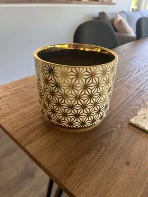 Guldig kruka med geometriskt mönster - Snygg kruka i keramik med guldfärgat geometriskt mönster och blank finish. Perfekt som inredningsdetalj för att ge rummet en lyxig känsla. Rund form och passar bra till mindre växter eller som dekoration.