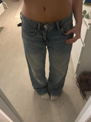 Blåa baggy jeans med låg midja - Säljer ett par blåa jeans med låg midja och raka ben. Jeansen har klassisk femficksdesign och är tillverkade i denim. Perfekta för en avslappnad och trendig look. Dem är från Pull&Bear, har kortat ner dem, passar 150-157 cm 