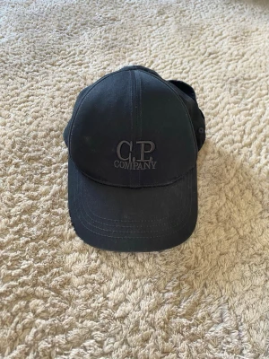 Svart keps från C.P. Company - Säljer min keps från cp company då jag tappat intresse. Den är sparsamt använd. Storlek: M (passar de flesta). Den är äkta köptes på nk för typ ett år sedan för ca 1100kr. Finns qr kod för att kolla äktheten.