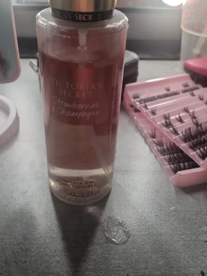 Victorias Secret Strawberries & Champagne - Fräsch body mist från Victorias Secret i doften Strawberries & Champagne. Flaskan är cylinderformad och genomskinlig med rosa vätska och guldfärgat lock. Rymmer 250 ml och har en elegant design med vit text på framsidan.