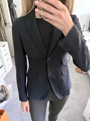 Svart figursydd kavaj med fickor - Snygg marinblå kavaj från Dondup med två knappar framtill och klassiska slag. Figursydd modell med två fickor med lock och dekorativa knappar vid ärmsluten. Storlek 38 men skulle säga att det mer är en 34/36. 100% ull. Nypris: 4000 kr