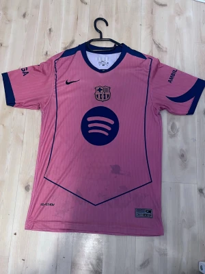 Rosa FC Barcelona matchtröja Nike - Snygg rosa FC Barcelona matchtröja med mörkblå detaljer och tryck. Tröjan har klubbmärke, Spotify-logga och nummer 19 med Lamine Yamal på ryggen. Korta ärmar, rund hals och tillverkad i lätt, andningsbart material. Perfekt för fotbollsträning eller att bära till vardags.
