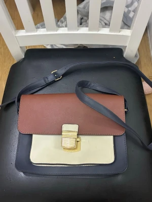 Trefärgad axelremsväska från Primark - Den här trefärgade axelremsväskan från Primark har ett strukturerat brunt lock och en guldtonad låsstängning. Helt ny.