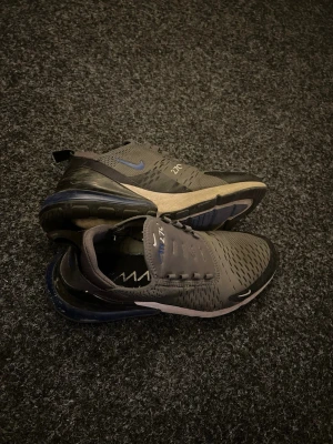 Nike Air Max 270  - Perfekta enda problemet är : Smutsiga asså har vit nånting men det går bort och ingen shoe lace annars helt nya köpte för 2300kr. Nike Air Max 270 sneakers i grått med blå detaljer och svart sula. Ovandelen är i mesh för bra ventilation och skon har en synlig Air-enhet i hälen för extra komfort. Snygg och sportig design med klassisk Nike-logga på sidan.