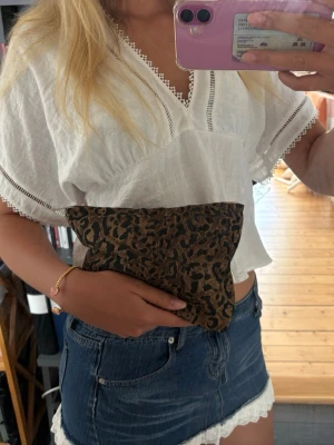 Leopardmönstrad liten väska - Säljer en liten väska med leopardmönster i brunt och svart. Väskan har dragkedja upptill och är tillverkad i ett tygmaterial. Perfekt för att bära småsaker eller använda som sminkväska. Enkel och trendig accessoar att ha med sig.