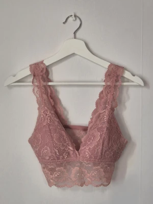 Rosa spetsbralette med bred kant - Säljer en superfin rosa bralette i spets med bred kant och blommigt mönster. Den har breda axelband och v-ringning både fram och bak. Perfekt för dig som gillar romantisk och feminin stil. Uppskattad storlek: S