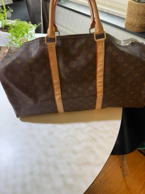 Louis Vuitton Keepall Monogram väska - Säljer en klassisk vintage Louis Vuitton Keepall resväska i brunt monogramcanvas med beigea läderdetaljer och handtag. Väskan har dragkedja upptill och ikoniskt LV-mönster över hela ytan. Perfekt för weekendresor och har en rymlig insida. Dragkedjan är trasig men går att fixa (sista bilden)