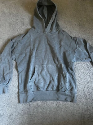 Grå hoodie med magficka - En stilren grå hoodie med stor huva och klassisk magficka framtill. Hoodien har ribbade muddar vid ärmslut och nederkant. Perfekt för en avslappnad och bekväm look. Materialet känns mjukt och passar bra till vardags. Vid frågor är de bara att skriva pris kan diskuteras 