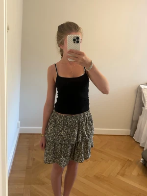 Blommig volangkjol i svart och vitt - Supersöt kort kjol med blommigt mönster i svart och vitt. Kjolen har volangdetaljer och en luftig passform som ger en avslappnad och trendig look. Perfekt för varma dagar och enkel att matcha med olika toppar.