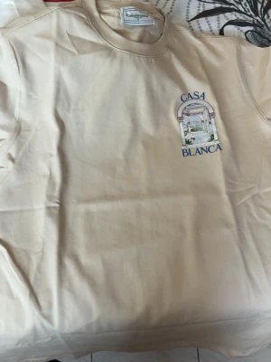 Beige sweatshirt från Casablanca - Snygg beige sweatshirt från Casablanca med tryck av ett klassiskt valv och texten 'Casa Blanca' både fram och stort på ryggen. Tröjan har rund hals och är tillverkad i mjukt bomullsmaterial. Perfekt för dig som gillar stilrena plagg med unik design.