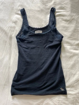 Mörkblått spetslinne från abercrombie - Snyggt mörkblått linne från abercrombie med axelband i spets och liten broderad logga nertill. Storlek L-kids men passar mig som har XS- S! Perfekt att styla till jeans eller kjol.💞
