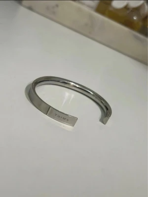 Silvrigt armband från Triwa - Stilrent armband i silverfärgad metall från Triwa. Öppen design som gör det enkelt att ta på och av. Armbandet har en minimalistisk och modern look med Triwa-loggan ingraverad på ena sidan. Perfekt accessoar för dig som gillar enkel men snygg stil.