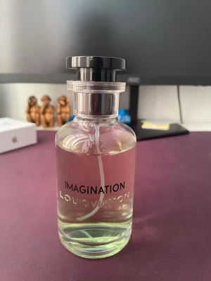  Imagination parfym - Exklusiv parfym från med namnet Imagination. Flaskan är genomskinlig med svart lock och stilren design. Parfymen har en ljus, nästan transparent färg och flaskan är i glas med tryckt text framtill.