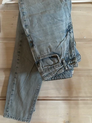 Ljusblå raka jeans vintage-look - Säljer ett par ljusblå jeans med rak passform och klassisk femficksdesign. Jeansen har en avslappnad vintage-känsla och är tillverkade i denim. Perfekta för en casual och trendig stil.