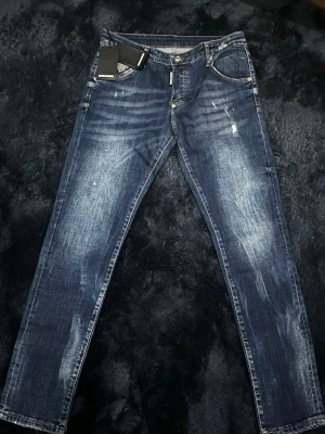 Mörkblå Dsquared2 jeans  - Snygga mörkblå Dsquared2 jeans med slim fit passform och coola slitningar samt ljusa tvättade detaljer. Klassisk femficksmodell med knappgylf. Perfekta för en trendig och avslappnad look. Och pris kan diskuteras.