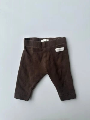 Bruna leggings från Newbie strl 56 - Mörkbruna leggings från Newbie i mjuk bomull. Klassisk rak passform med resår i midjan och diskret logga framtill. Perfekta för en chill och enkel look till de allra minsta.