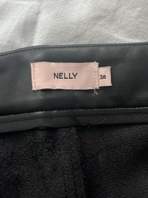 Svarta utsvängda byxor från Nelly - Snygga svarta byxor i fuskskinn från Nelly med utsvängda ben och hög midja. Materialet ger en cool look och passar perfekt till en trendig outfit. Byxorna har en slät finish och sitter tajt upptill för en smickrande siluett.