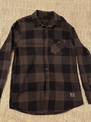 Rutig skjorta  - Rutig skjorta i grått från Skill Casual Wear. Skjortan har klassisk krage, bröstficka och knappar framtill. Jag är 174 och den sitter lagom på mig.