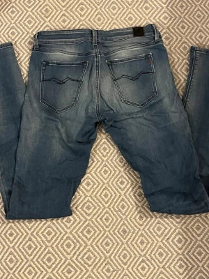 Slim fit Replay Jeans - Schysstare Replay jeans med en snygg tvätt med en klassisk femficksmodell och coola kontrastsömmar på bakfickorna. Jeansen har en liten ficka fram med Replay-logga i rött och är tillverkade i slitstark denim. Perfekta för en avslappnad och trendig look. Slim fit modell, kontakta om intresse!