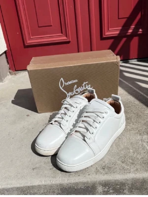 Vita Christian Louboutin sneakers - Snygga vita sneakers från Christian Louboutin med klassisk röd sula och vita skosnören. Skorna är låga och har en stilren design i läder med diskreta detaljer. Perfekta för dig som vill ha en clean look med exklusiv känsla.