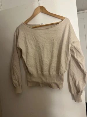 Off-shoulder topp - Säljer en beige stickad off shoulder top. Tröjan har ribbade muddar vid ärmslut och midja, och är tillverkad i ett mjukt material som passar perfekt till vardagslooken. Är endast använd ett fåtal gånger. 