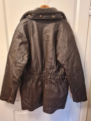 Mörkbrun skinnjacka med fårkrage - Säljer en mörkbrun skinnjacka från Euro Leathers med fårskinnsliknande krage. Jackan har flera dragkedjeförsedda fickor, justerbar midja och detaljer i metall. Perfekt för dig som vill ha en klassisk och tidlös look.