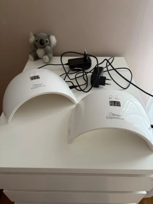 Nagellampa från Nagelgiganten.se - Säljer två vita nagellampor från Nagelgiganten.se med digital display och timerfunktion. Perfekta för att härda gelélack och andra nagelprodukter. Båda lamporna har en halvbågad form och drivs med medföljande strömadapter.